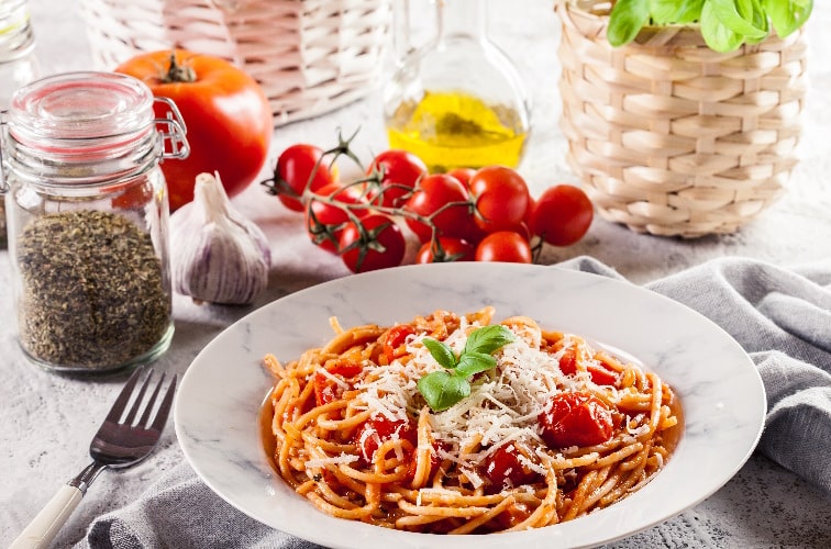 Spaghetti Napoli Rezept am Tisch serviert mit Oregano und Cocktailtomaten sowie Parmesan